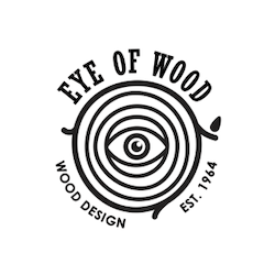 Logo of Eye of Wood showing a tree ring with an eye at the center. The text reads Eye of Wood at the top and Wood Design with Est. 1964 below. The design is black on a white background.