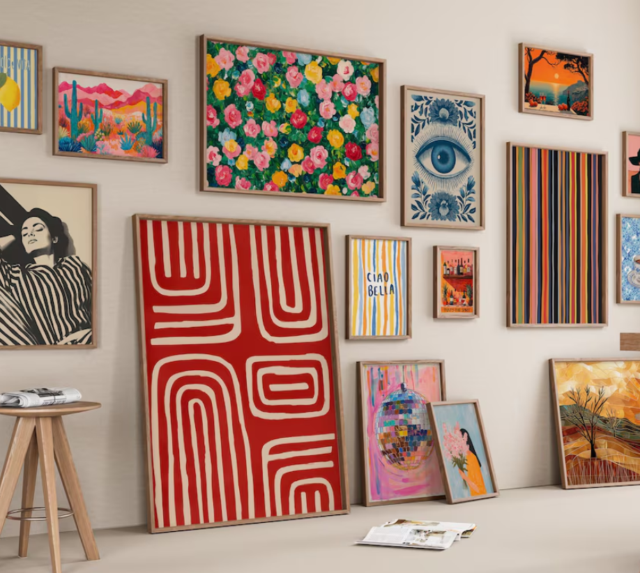 A gallery wall featuring colorful framed art—including abstract patterns, florals, a blue eye, landscapes, and a black and white portrait—offers great Digital Download Ideas for anyone seeking the best digital products to sell. Some pieces rest casually on the floor.